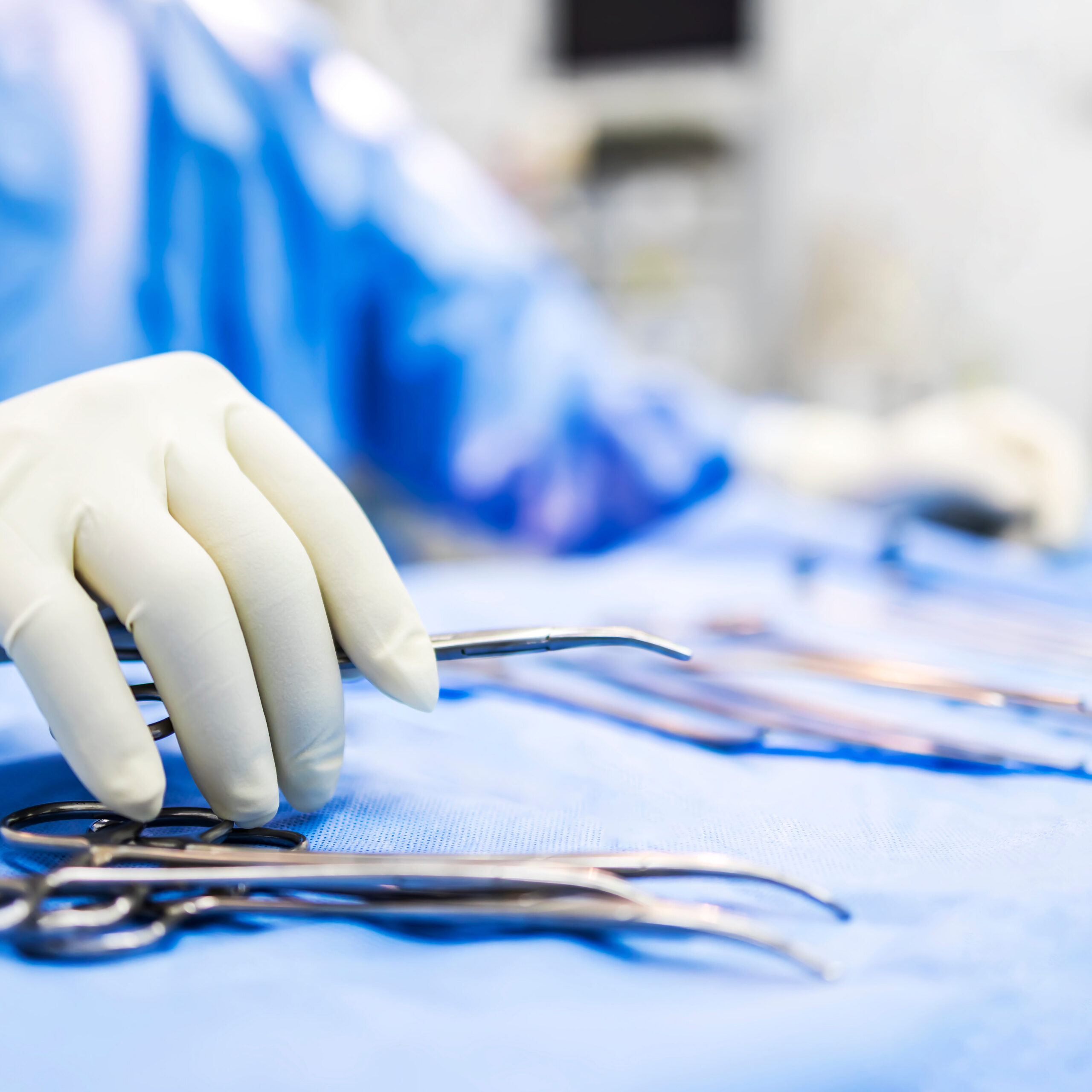 Hand of doctor or surgeon in blue gown pick up surgical clamp instrument or tools inside operating theatre with blur background.Medical equipment for surgery inside room in hospital.Modern technology. Primo piano di un veterinario che prende degli strumenti chirurgici durante un intervento